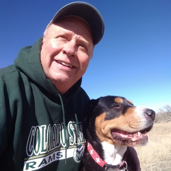 Steve-D-person-smiling-wearing-a-hat-outside-with-dog person outside, smiling and wearing a hat, their arm around a dog